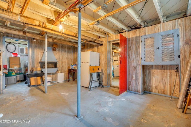 unfinished below grade area featuring wooden walls and freestanding refrigerator