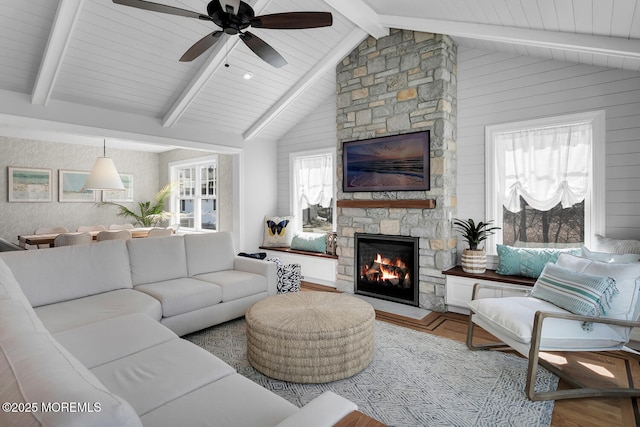 living room featuring a stone fireplace, wood finished floors, vaulted ceiling with beams, and a ceiling fan