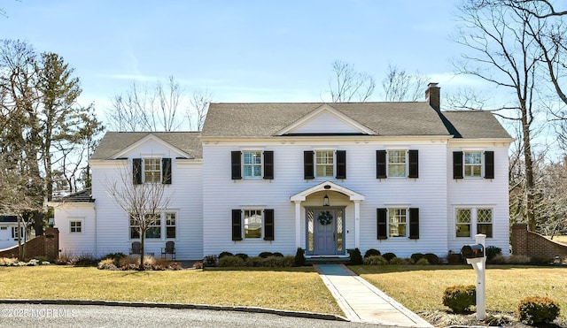 colonial home with a chimney, a front lawn, and roof with shingles