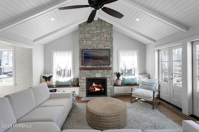 living room featuring a stone fireplace, lofted ceiling with beams, ceiling fan, and wood finished floors