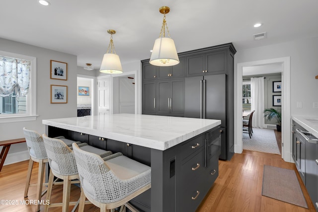 kitchen with light wood-type flooring, visible vents, decorative light fixtures, a kitchen island, and light stone countertops