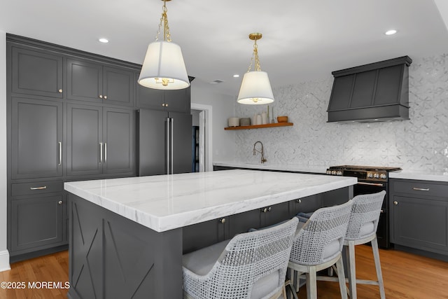 kitchen featuring custom range hood, light stone counters, a kitchen island, light wood-style floors, and appliances with stainless steel finishes