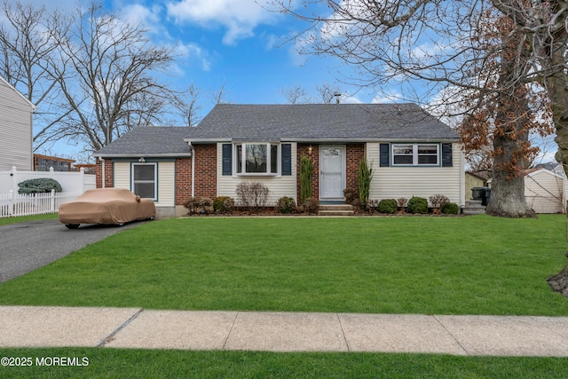 view of front facade with a front lawn, fence, brick siding, and roof with shingles