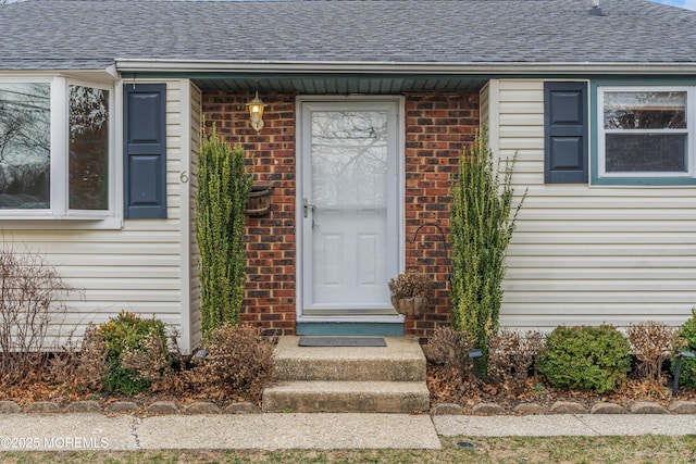 view of exterior entry featuring brick siding and roof with shingles