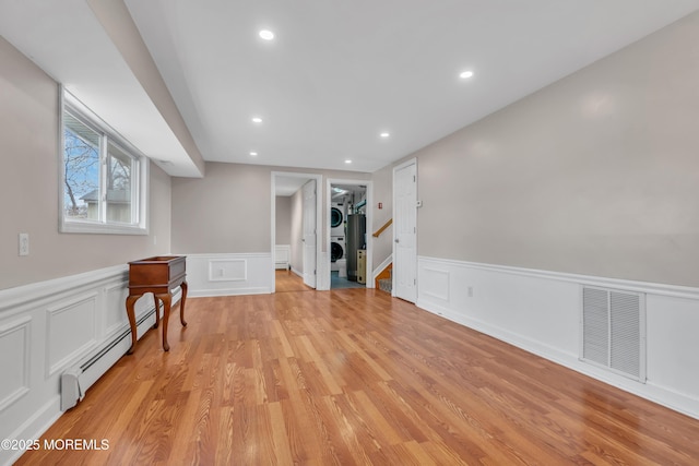 basement with stacked washer / dryer, visible vents, recessed lighting, light wood-style floors, and a baseboard radiator