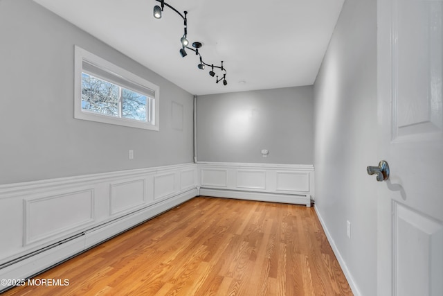 spare room with wainscoting, light wood-style flooring, rail lighting, and a baseboard radiator