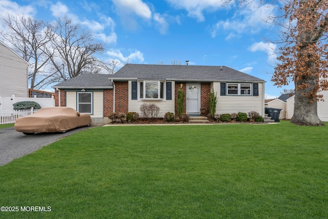 single story home featuring brick siding, a shingled roof, a front lawn, and fence