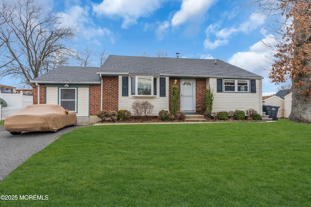 ranch-style home with brick siding, a front yard, roof with shingles, and fence