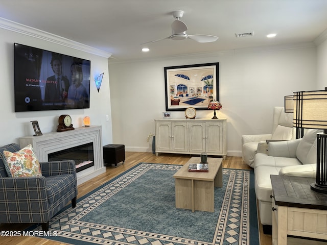 living room with visible vents, a ceiling fan, wood finished floors, crown molding, and baseboards