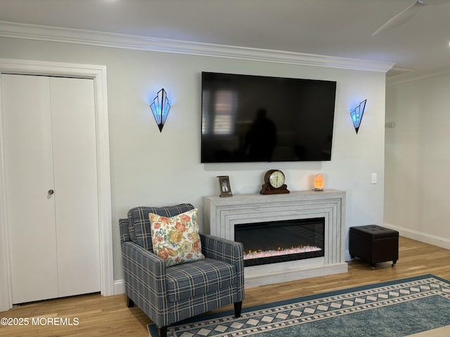 sitting room featuring a glass covered fireplace, baseboards, wood finished floors, and ornamental molding