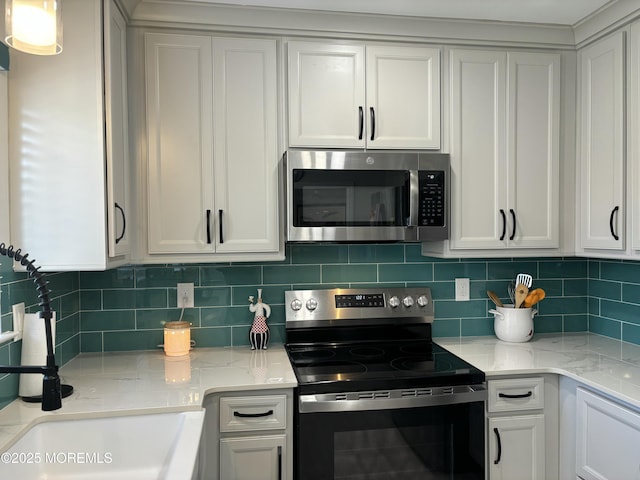 kitchen featuring backsplash, light stone counters, appliances with stainless steel finishes, white cabinetry, and a sink