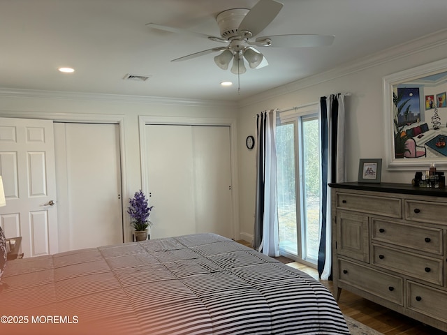 bedroom with visible vents, crown molding, ceiling fan, dark wood-type flooring, and multiple closets