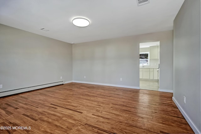 empty room featuring visible vents, a sink, a baseboard heating unit, wood finished floors, and baseboards