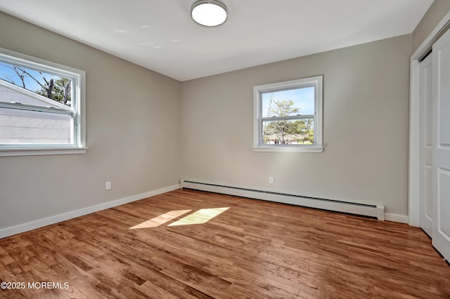 unfurnished bedroom featuring a baseboard heating unit, multiple windows, baseboards, and wood finished floors