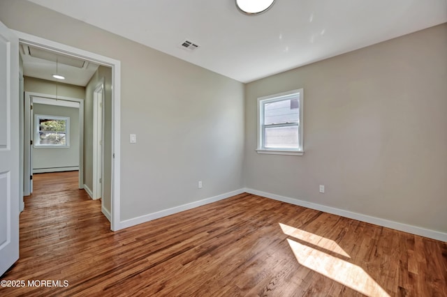 spare room with wood finished floors, visible vents, a healthy amount of sunlight, attic access, and baseboard heating