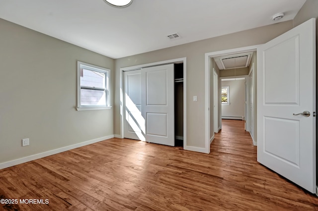 unfurnished bedroom with visible vents, multiple windows, attic access, and a baseboard radiator