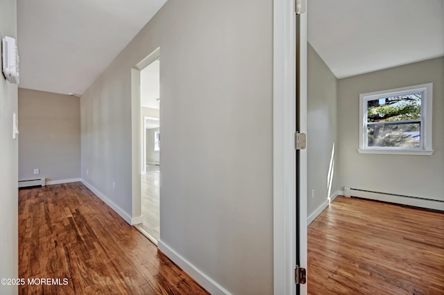 corridor featuring a baseboard heating unit, wood finished floors, and baseboards