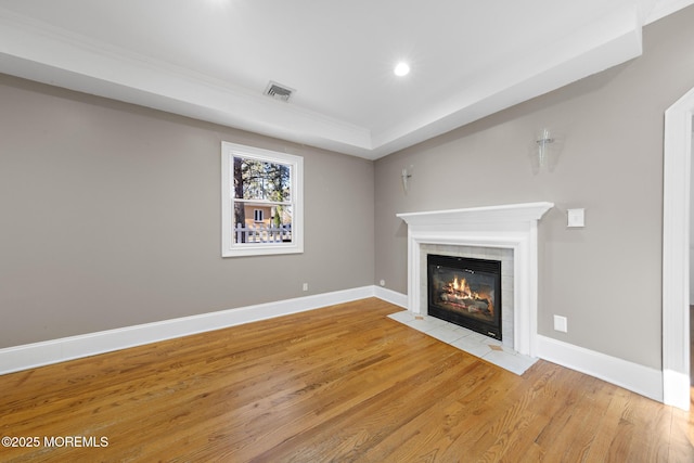 unfurnished living room featuring a tiled fireplace, baseboards, visible vents, and light wood finished floors