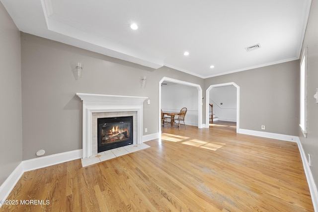 unfurnished living room with arched walkways, visible vents, light wood finished floors, and ornamental molding