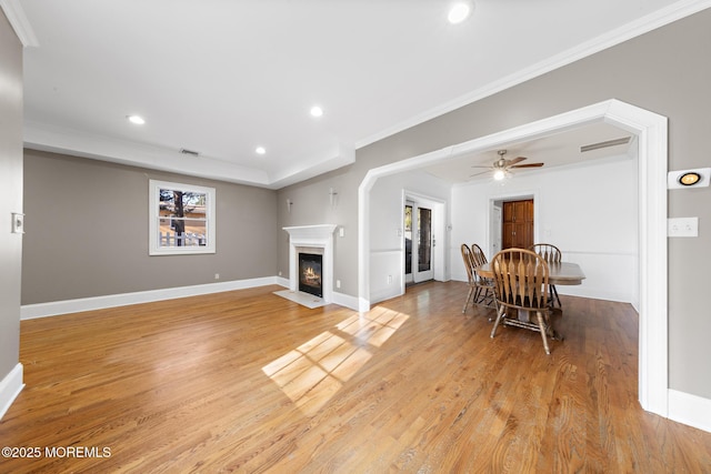 living room with visible vents, baseboards, a fireplace with flush hearth, ornamental molding, and light wood-style floors