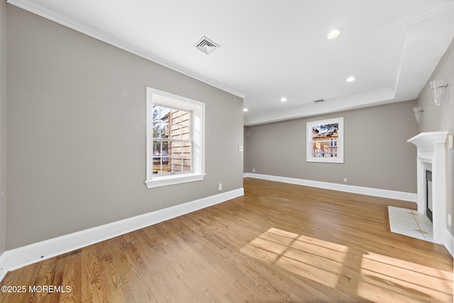 unfurnished living room with wood finished floors, visible vents, baseboards, a fireplace with flush hearth, and ornamental molding