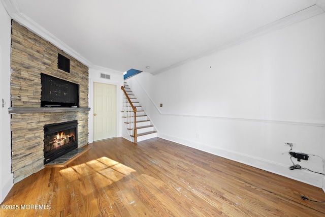 unfurnished living room featuring wood finished floors, visible vents, stairs, a stone fireplace, and crown molding