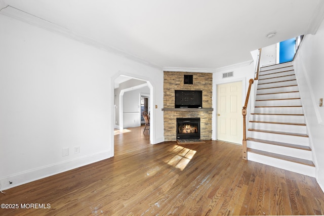 unfurnished living room with visible vents, wood finished floors, stairway, a stone fireplace, and crown molding