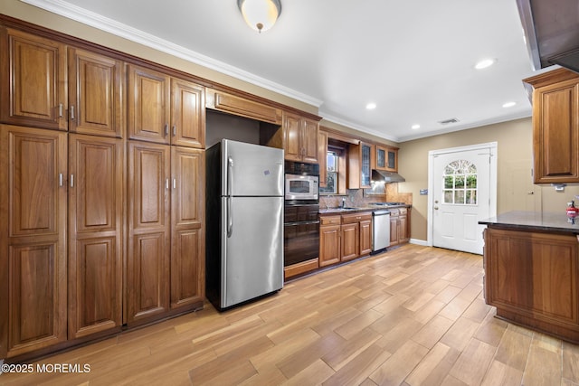 kitchen with under cabinet range hood, decorative backsplash, brown cabinets, and stainless steel appliances