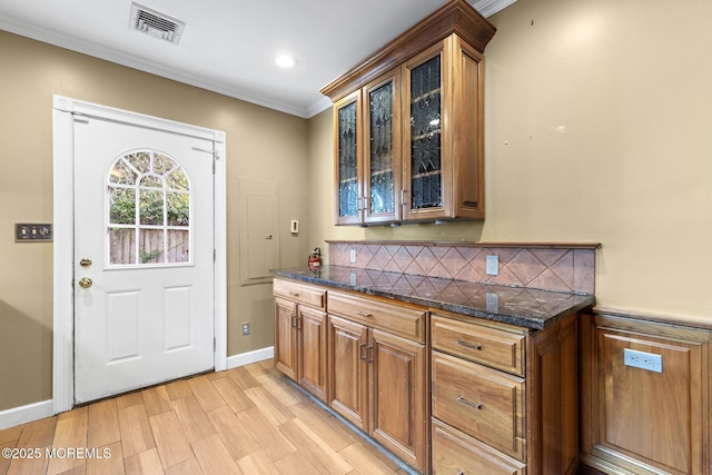 kitchen with visible vents, light wood-type flooring, glass insert cabinets, crown molding, and tasteful backsplash