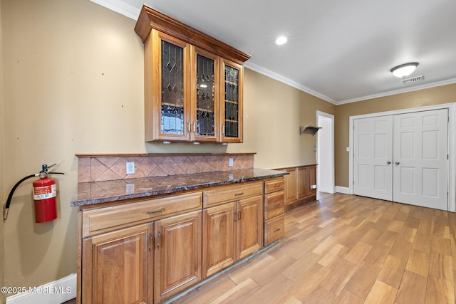 kitchen featuring light wood-style flooring, glass insert cabinets, and ornamental molding