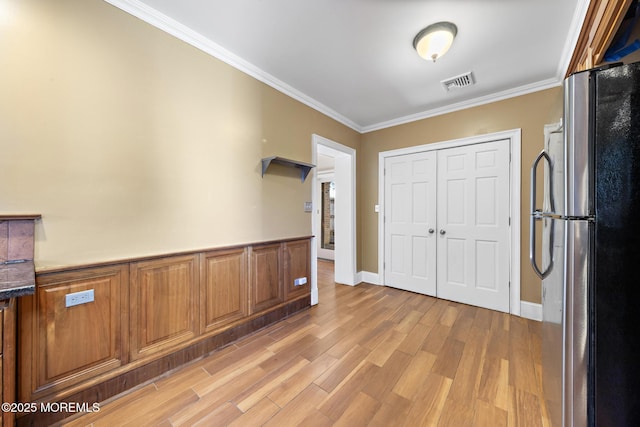 entryway with wainscoting, light wood-style floors, visible vents, and ornamental molding