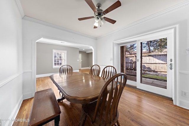 dining area with ornamental molding, a ceiling fan, wood finished floors, arched walkways, and baseboards