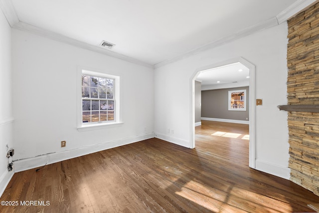 empty room featuring visible vents, crown molding, baseboards, and wood finished floors