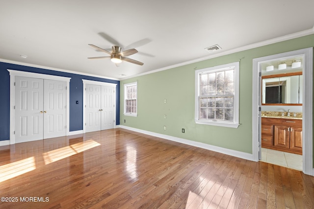 unfurnished bedroom with visible vents, multiple closets, a sink, crown molding, and light wood finished floors