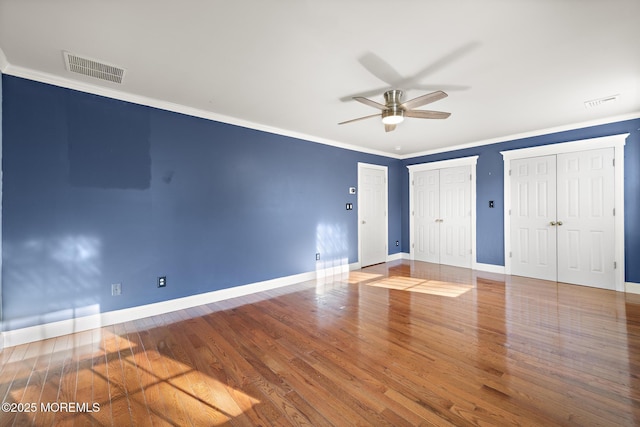 unfurnished bedroom featuring visible vents, two closets, baseboards, ornamental molding, and wood finished floors