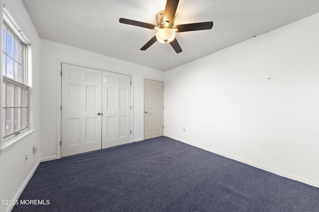 unfurnished bedroom with a closet, baseboards, ceiling fan, and dark carpet