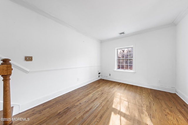 spare room with visible vents, wood finished floors, baseboards, and ornamental molding