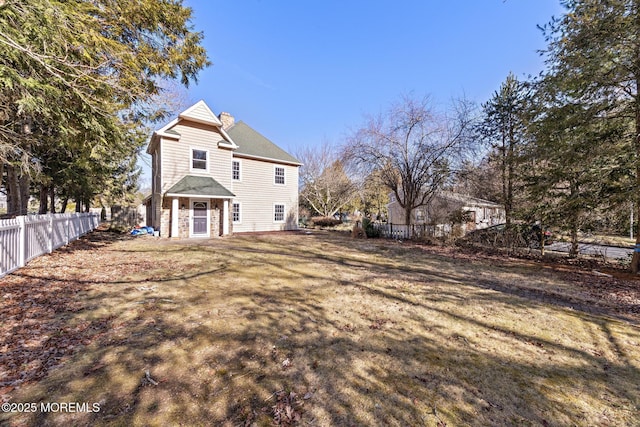 rear view of house with fence, a lawn, stone siding, and a chimney