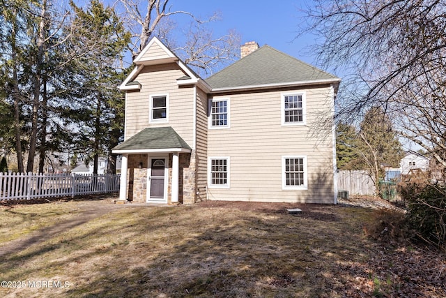 back of house with fence, stone siding, roof with shingles, and a chimney