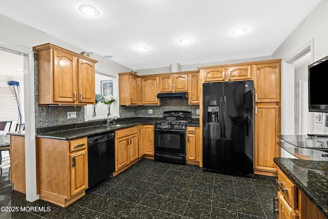 kitchen featuring tasteful backsplash, under cabinet range hood, dark stone countertops, black appliances, and a sink