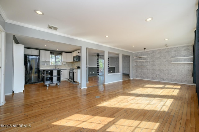 unfurnished living room featuring light wood-type flooring, brick wall, and crown molding