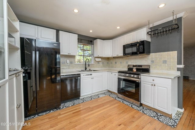 kitchen with light countertops, light wood-style flooring, white cabinets, black appliances, and a sink