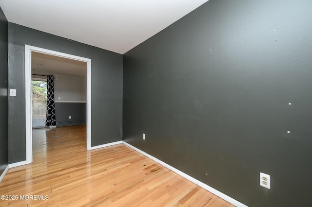 unfurnished room with a baseboard heating unit, light wood-style floors, and baseboards