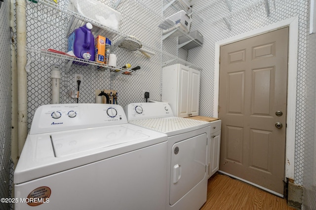 washroom featuring washing machine and clothes dryer, cabinet space, and light wood finished floors