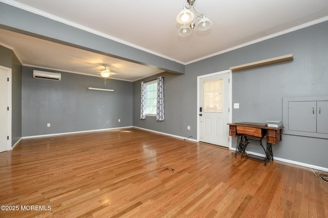 unfurnished living room with light wood-style flooring, ornamental molding, ceiling fan with notable chandelier, a wall mounted AC, and baseboards