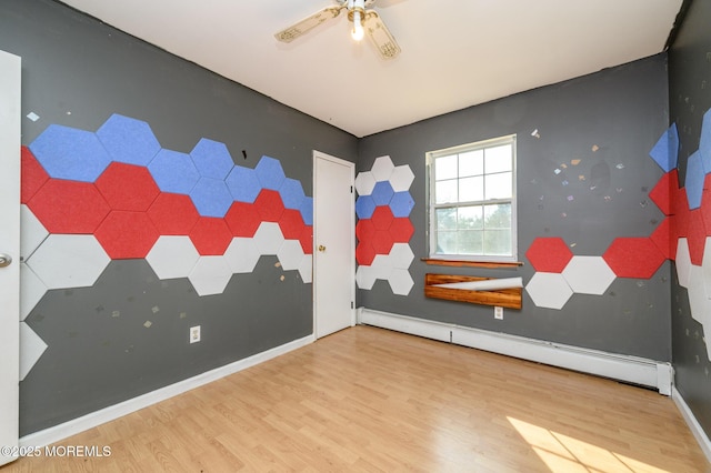 spare room with a baseboard heating unit, wood finished floors, baseboards, ceiling fan, and an accent wall