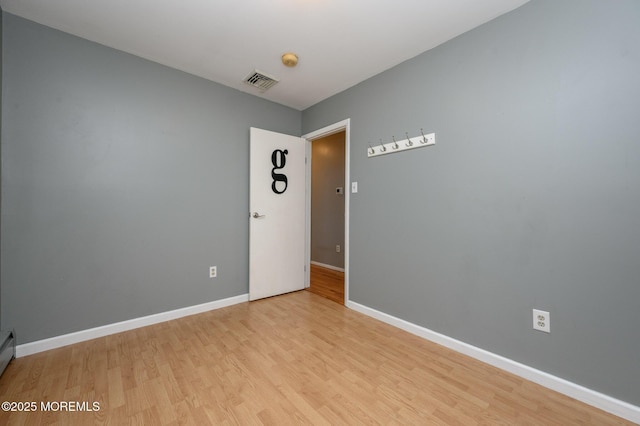 empty room featuring visible vents, light wood-style flooring, baseboard heating, and baseboards