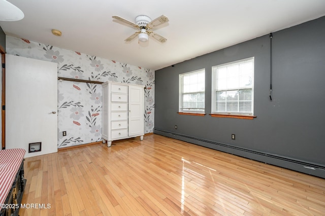 unfurnished bedroom with wallpapered walls, baseboards, light wood-type flooring, a ceiling fan, and a baseboard radiator