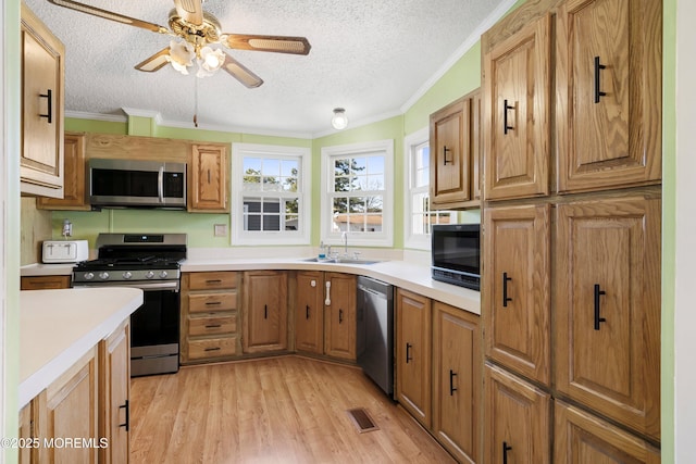 kitchen with light wood-type flooring, visible vents, a sink, stainless steel appliances, and crown molding