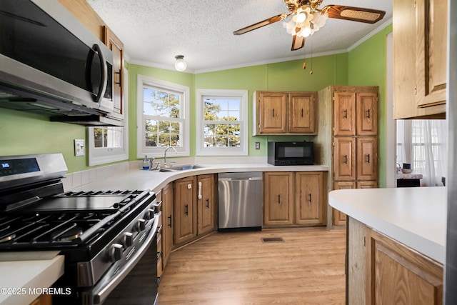 kitchen with stainless steel appliances, crown molding, light wood-style floors, and a sink